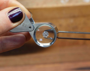 Brilliant Round 1 Carat Diamond held in fine nose tweezers being viewed through a loupe