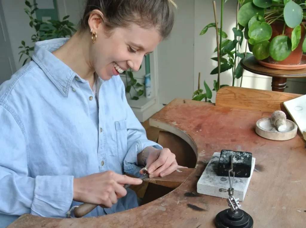 Genevieve Schwartz smiling whilst working on a ring at her workbench