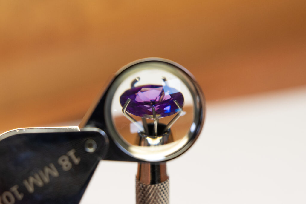Round cut faceted stone held in grabber and viewed through a loupe - gemmology for beginners